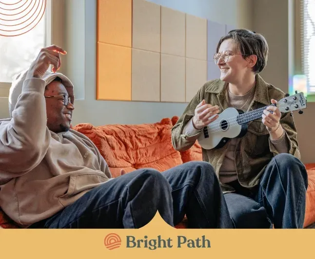 Two people sharing music on a ukulele in a Bright Path group room
