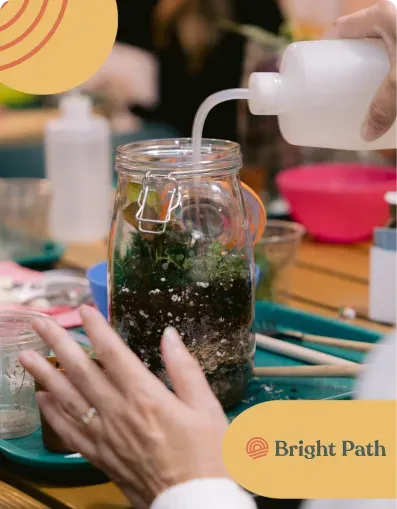 Hands watering a terrarium during a horticultural therapy activity at Bright Path