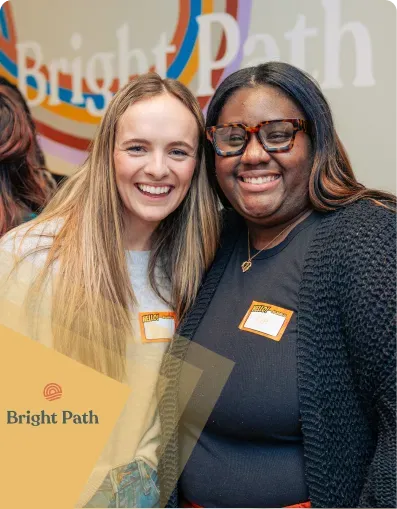 Two smiling women with name tags in front of the Bright Path wall sign