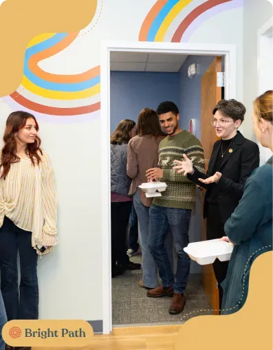 Guests talking in a doorway beside a rainbow wall mural at a Bright Path event