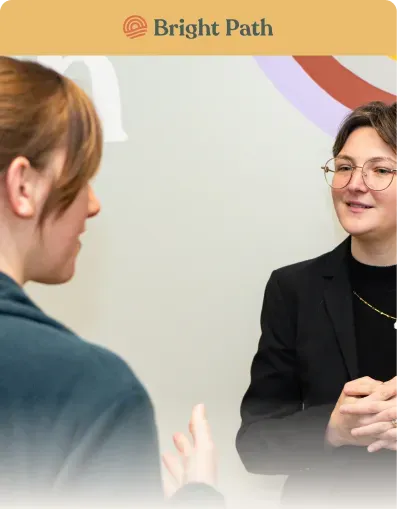 Two women talking beside a pastel wall graphic at Bright Path