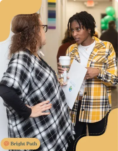 Two women talking at a Bright Path event, one holding a printed handout