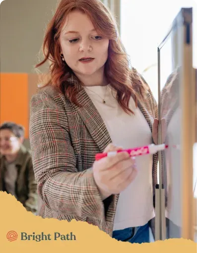 Woman writing on a whiteboard with a pink marker at Bright Path
