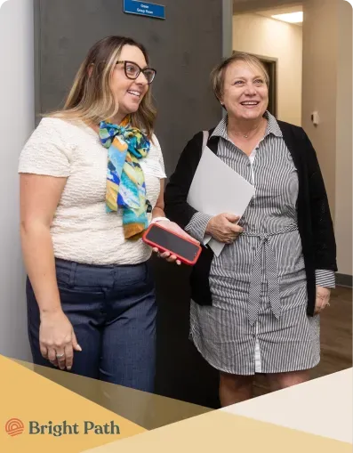 Two women smiling in a Bright Path hallway beside a group room door