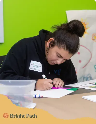 Teen drawing with markers at a table in front of a bright green wall at Bright Path