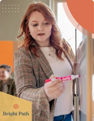 Woman writing on a whiteboard with a pink marker at Bright Path