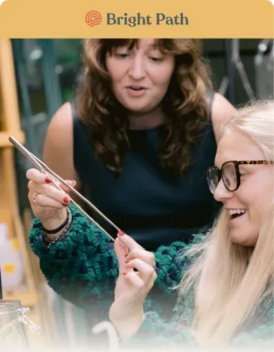 Woman holding long tweezers over a terrarium while another woman laughs at Bright Path