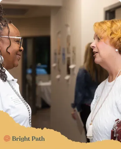Two women talking in a Bright Path hallway during a community event