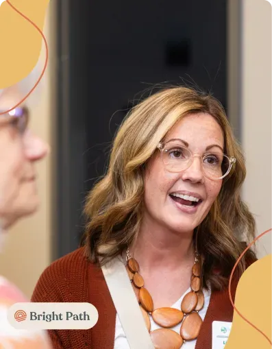 Smiling woman with glasses and an orange bead necklace at a Bright Path gathering