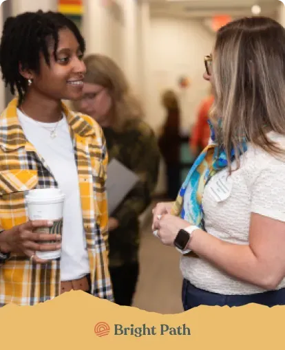 Two women talking in a Bright Path hallway, one holding a coffee cup