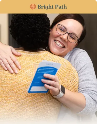 Smiling woman hugging a visitor who holds a Bright Path brochure