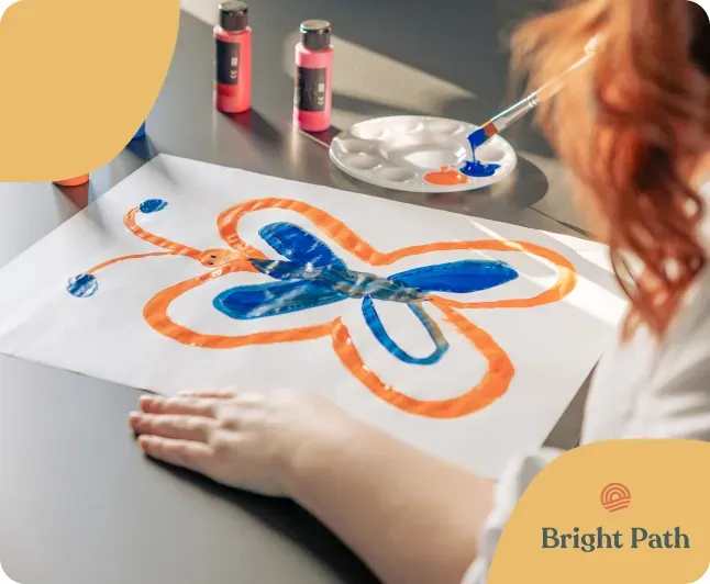 A young person painting an orange and blue butterfly with acrylic paints at a Bright Path art table