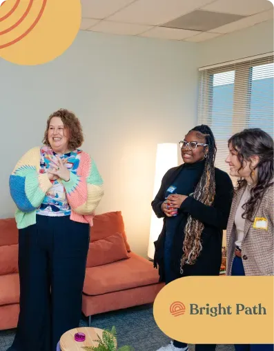 Three Bright Path staff members talking beside an orange sofa