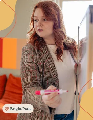 Woman writing on a whiteboard with a pink marker at Bright Path