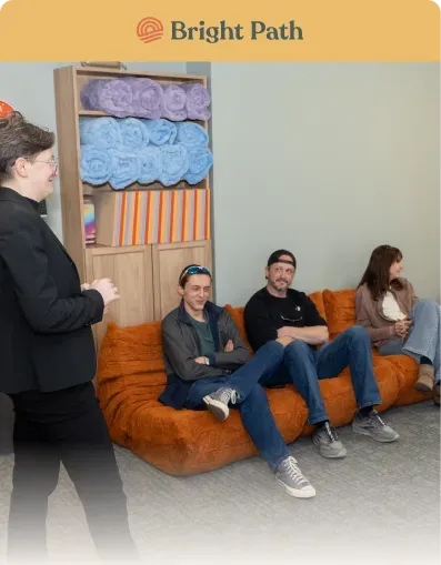 Woman speaking to three people seated on an orange floor couch in a Bright Path group room
