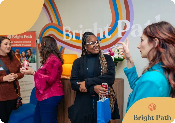 Women talking in front of the Bright Path rainbow wall sign, one holding a blue gift bag