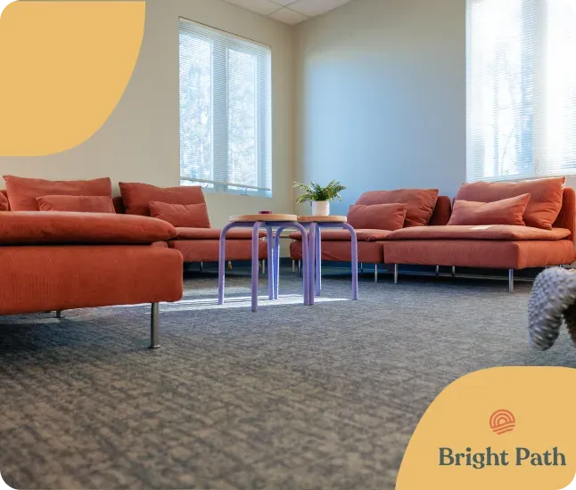 Bright Path lounge with coral sectional sofas, lilac side tables and tall bright windows