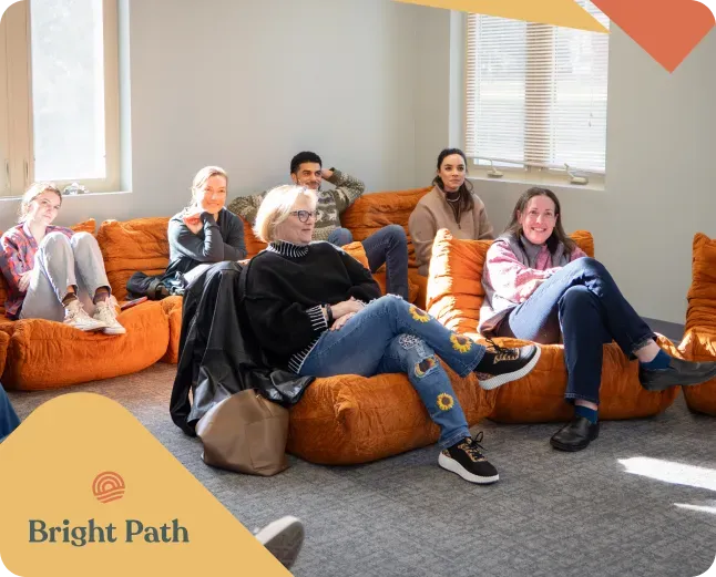 Seven adults seated on orange lounge sofas in a sunlit room, with the Bright Path logo in the corner