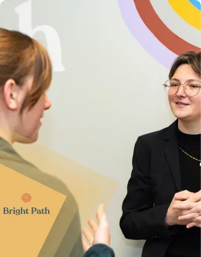 Two women in conversation beside a rainbow Bright Path wall graphic