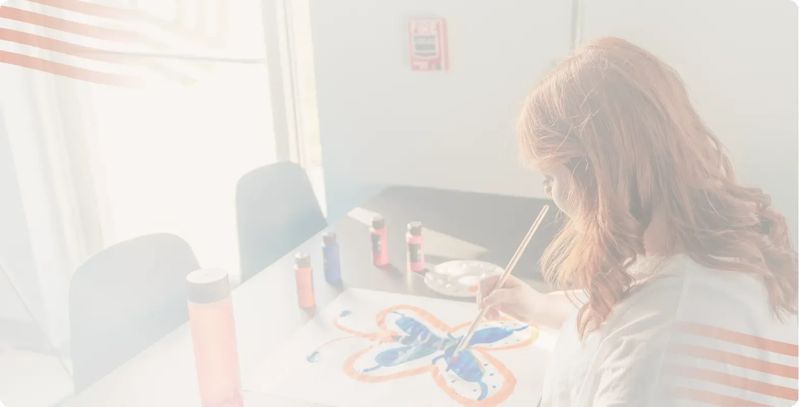 Teen with red hair painting a blue butterfly at a table, an art activity at Bright Path Behavioral Health