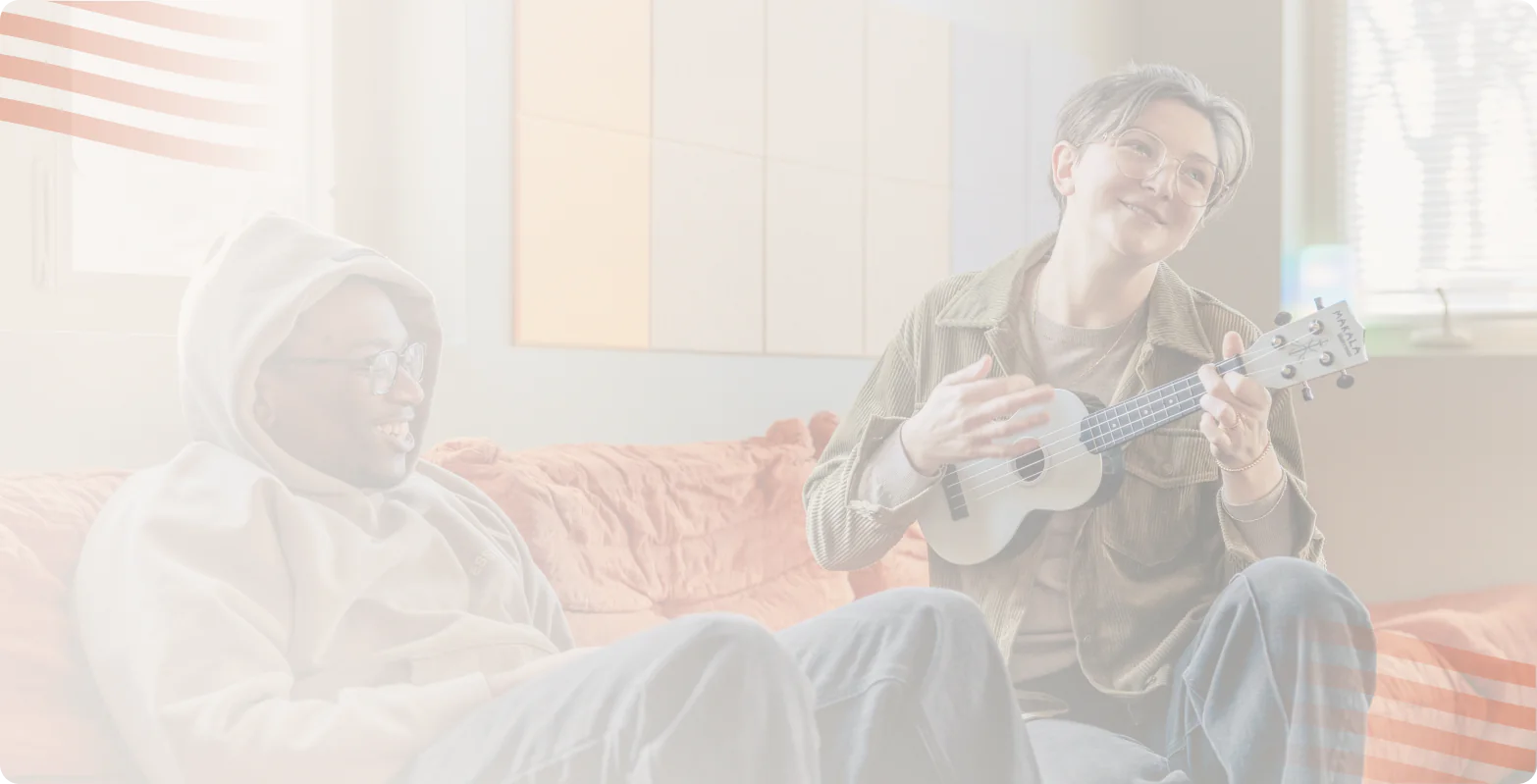 Two teens laughing on an orange couch while one plays a ukulele, Bright Path teen mental health treatment near Charlotte, NC