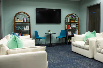 Wider view of the Wake Forest lounge with white sofas, mint pillows and a wall-mounted TV